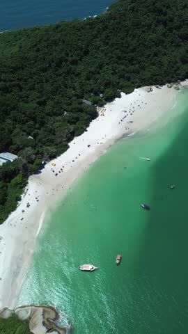 Drone aerial footage of Ilha do Campeche featuring tropical forest, turquoise ocean water, white sand beach and boats near Florianopolis in Santa Catarina, Brazil.