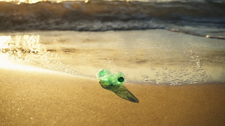 Plastic bottle left on sandy beach near sea waves during sunset, promoting awareness about waste reduction, sustainable lifestyle, and environmental responsibility.
