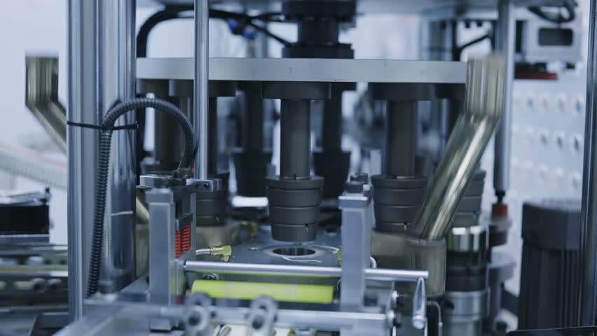 Close up of automated pharmaceutical filling system operating in advanced manufacturing facility. Precision industrial equipment used for medical packaging and production testing.