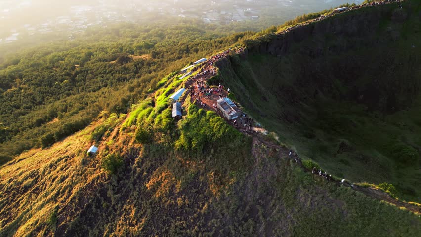 Rugged mountain spine curving around volcanic caldera with hikers exploring golden sunrise above forested slopes and dramatic mountain landscape overhead drone footage.