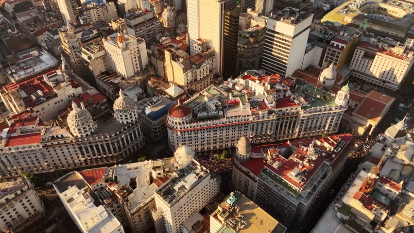 Crowds marching on streets towards Plaza de Mayo for university protest at golden hour in Buenos Aires, Argentina. Aerial top-down view