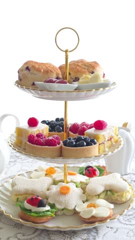 Summer theme afternoon tea tray with scones, desserts with fresh berries and flower, ladybug and butterfly finger sandwiches and crostini. Vertical handheld panning video.