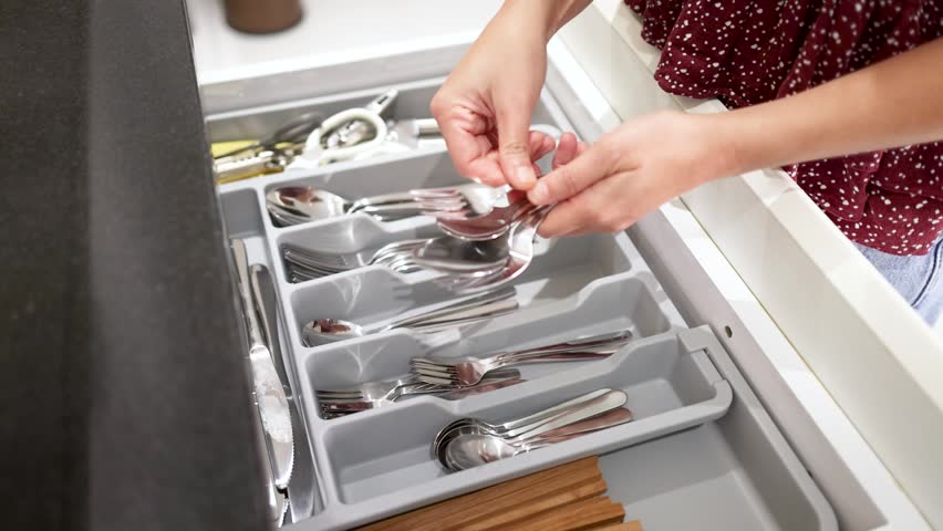 A person sorts forks and spoons into a grey plastic tray inside a kitchen drawer
