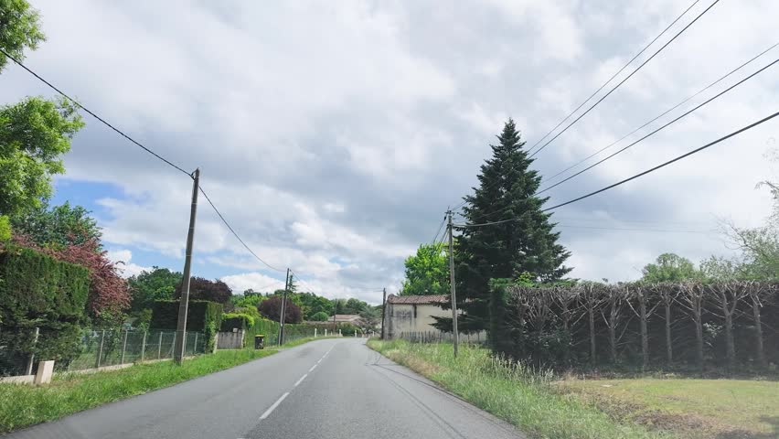 A vehicle travels along a paved road past stone houses and lush green trees