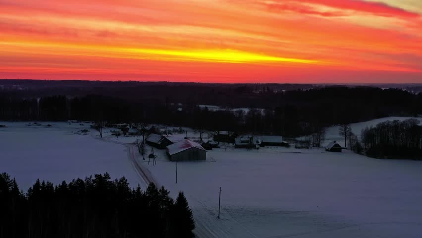 Winter landscape at sunset, vibrant orange and yellow sky over snowy fields, wide aerial view