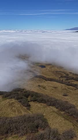 Breathtaking view of white clouds rolling over a mountain summit in the countryside. 