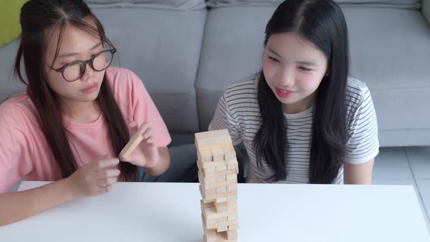 Two Asian girls playing Jenga board game togther in living room.