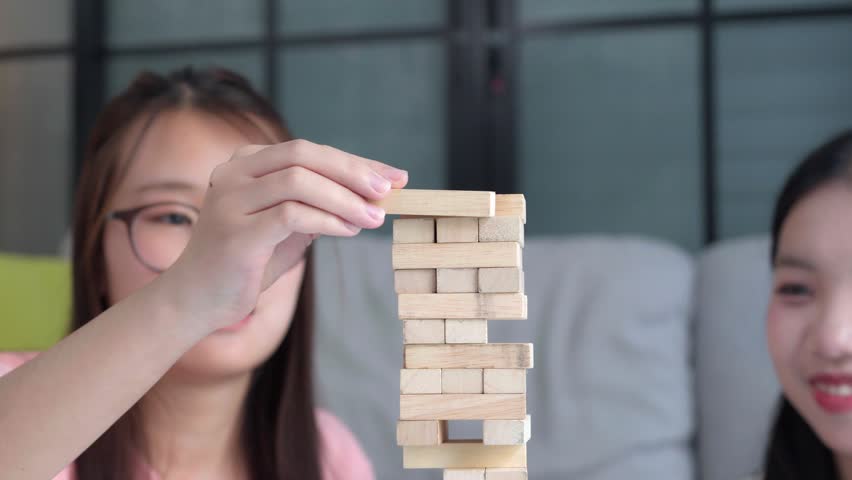 Two Asian girls playing Jenga board game togther in living room.