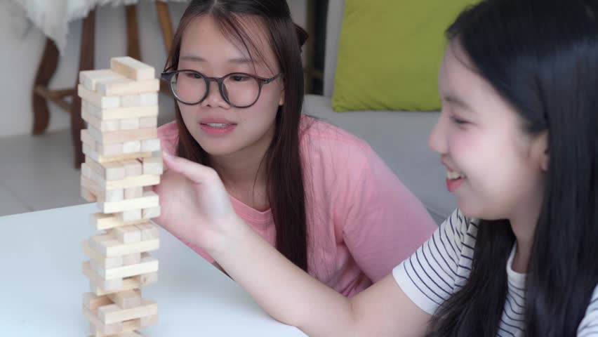 Two Asian girls playing Jenga board game togther in living room.