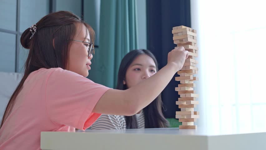 Two Asian girls playing Jenga board game togther in living room.