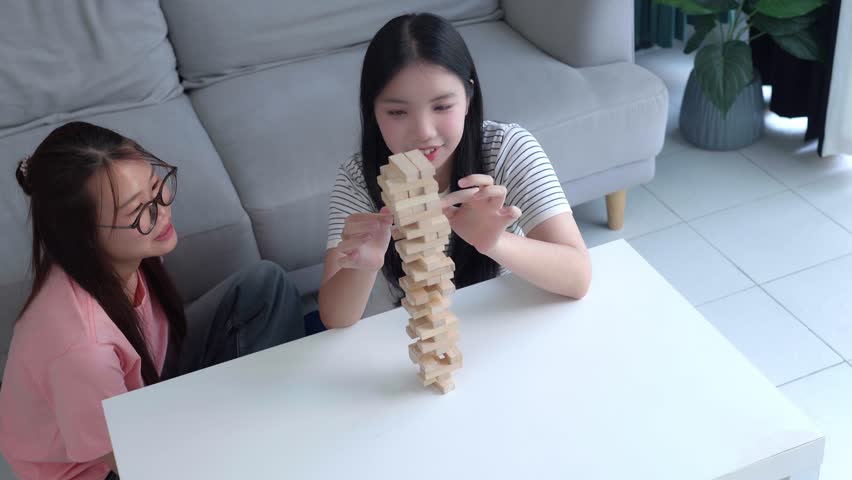 Two Asian girls playing Jenga board game togther in living room.