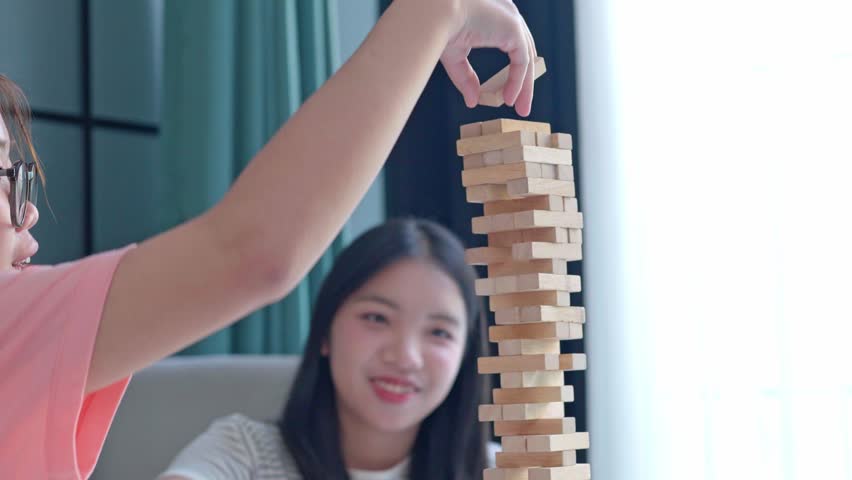 Two Asian girls playing Jenga board game togther in living room.