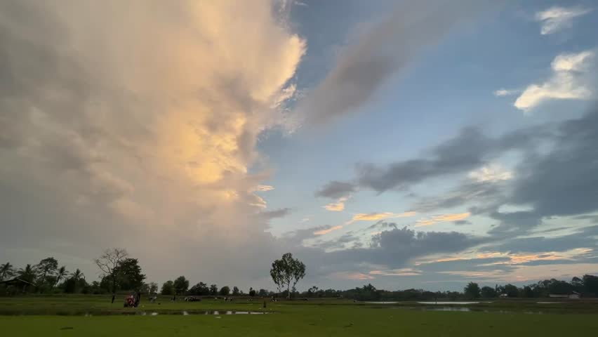 Scenic footage of a dramatic two tone sunset sky with contrasting golden and blue clouds above a peaceful green landscape. Natural countryside atmosphere with vibrant evening light and wide open horizon.