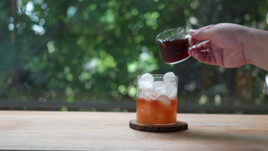 Hand pour shot of coffee into iced orange juice juice with ice