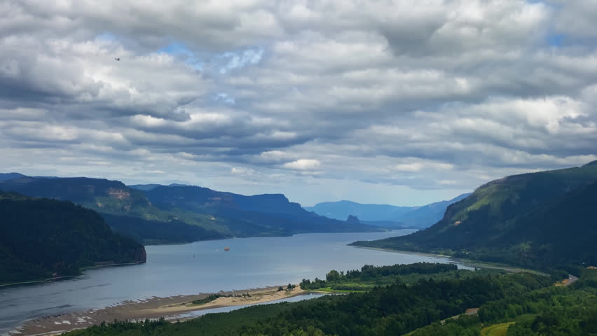 Panoramic Columbia River Gorge landscape with winding river and forested mountains under dramatic clouds