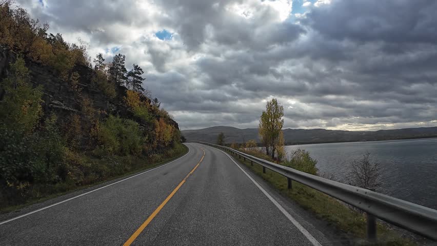 Point of view driving on a winding road along a fjord in Norway during a cloudy autumn day