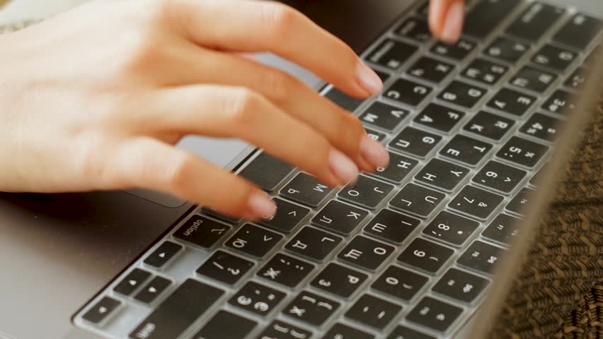 Human hands type on modern gray MacBook laptop keyboard, fingers pressing keys through a clear protective cover.