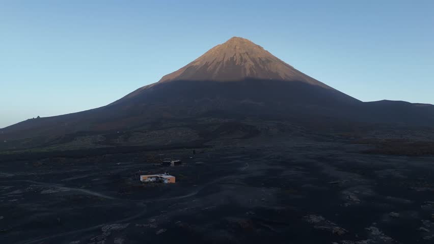 Majestic aerial view of the symmetrical Pico do Fogo volcanic cone in Cabo Verde, rising from the dark lava plains of the Chã das Caldeiras under a clear sky