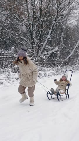 Family sledding in winter. outdoor winter activity. Happy, laughing, playful children are enjoying of sledging on snowy road, in forest, during snowfall. kids are having fun on snowy winter day