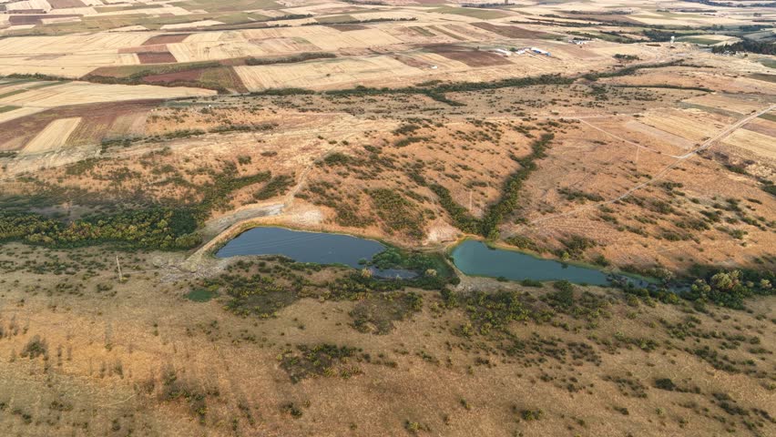 Small pond surrounded by open agricultural land, cultivated fields, and natural rural scenery. Captured from above, this footage highlights the harmony between water resources, farmland, and the quiet beauty of the countryside.