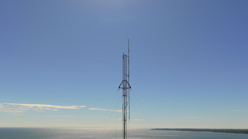 A tall communication tower stands prominently against a clear blue sky, with the Paraná River stretching out below. Ideal for telecommunications or infrastructure projects.