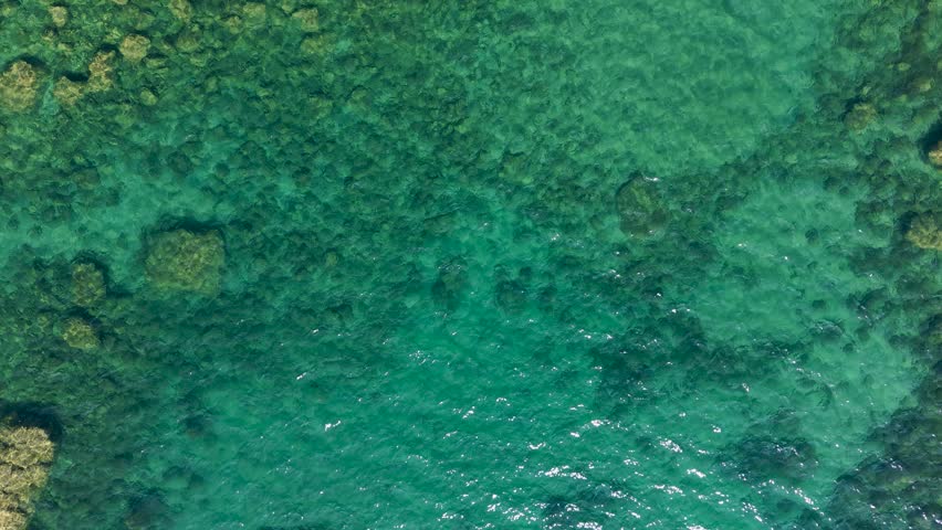 Top-down aerial view over turquoise freshwater reveals submerged boulders and the shadow of the drone gliding above the rocky shallows in Michigan