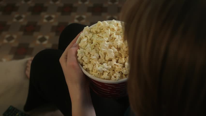 Woman watching TV series or movie at home while eating popcorn. Cozy evening entertainment and relaxation concept.