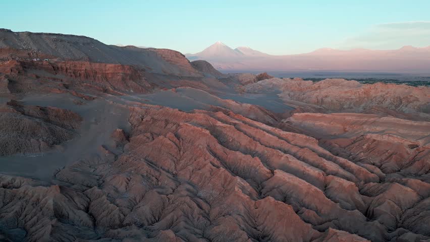 Orbit shot around Valle de la Luna eroded rock formations at dusk with snow-capped Licancabur volcano and pink twilight sky in the background. San Pedro de Atacama, Chile