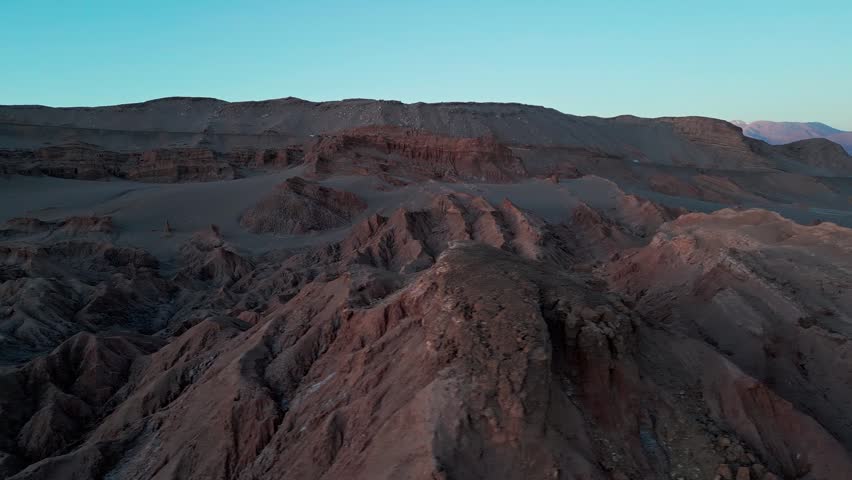 Orbit shot around Valle de la Luna dramatic eroded rock formations at dusk with snow-capped Licancabur volcano glowing in last twilight light under deep blue sky. San Pedro de Atacama, Chile