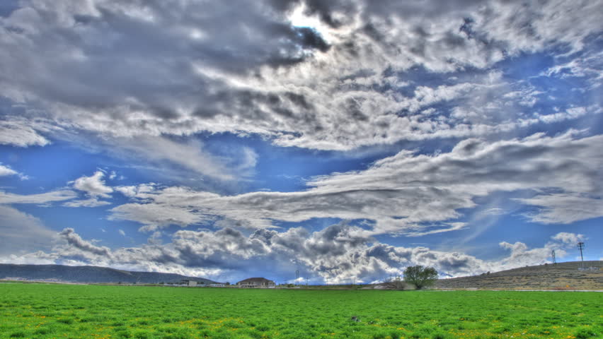 High definition tone mapped time lapse of cool clouds over a green field during