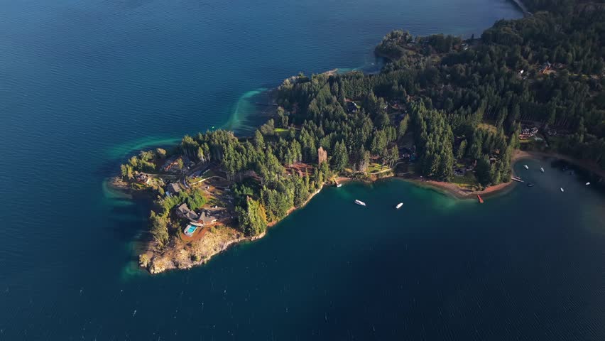 A breathtaking aerial perspective of a lush, forested peninsula extending into the deep blue waters of a Patagonian lake in Argentina.