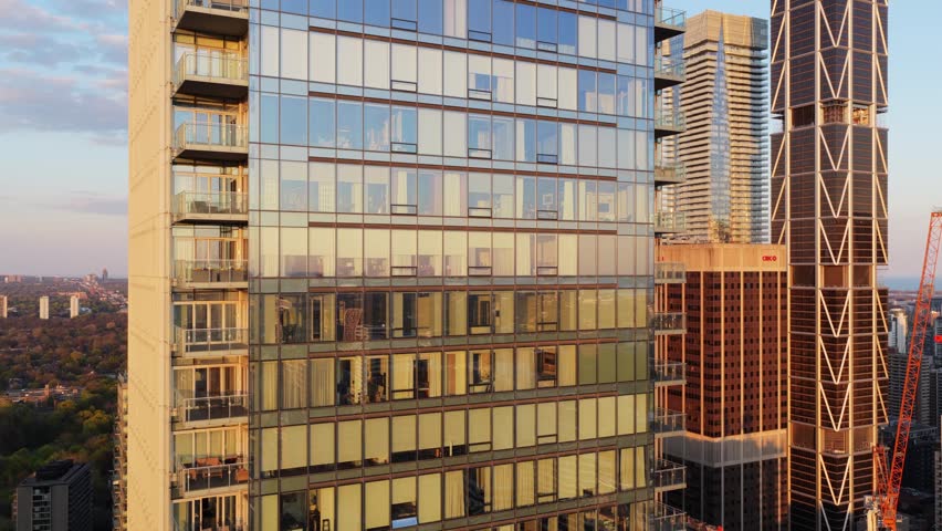 Modern residential tower facade with glass windows reflecting Toronto skyline at sunrise, urban architecture and apartments with balconies in downtown core