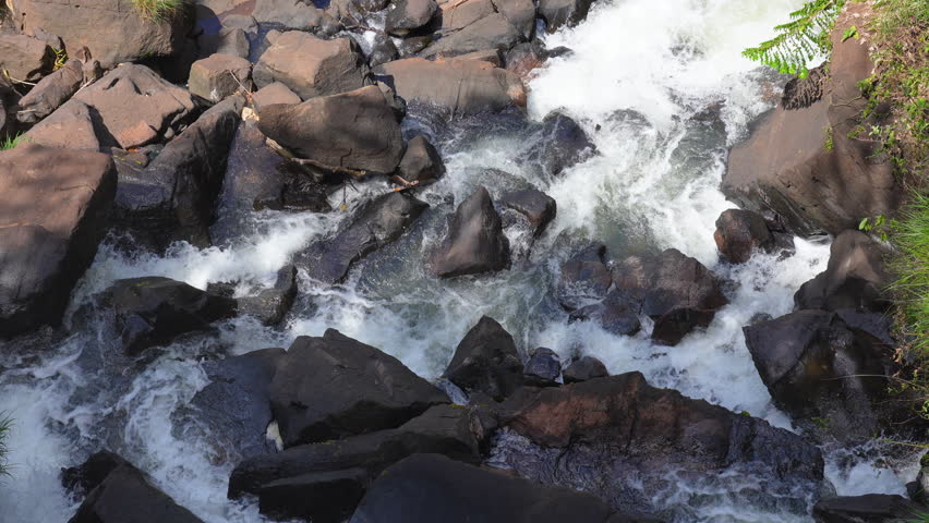 Top-down view of turbulent water flowing through large dark boulders at Iguazu Falls, capturing the dynamic energy of nature in a scenic rocky riverbed