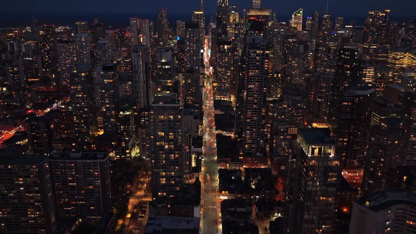 Pull back shot of nighttime Toronto cityscape with skyscrapers and illuminated streets retreating between modern glass buildings