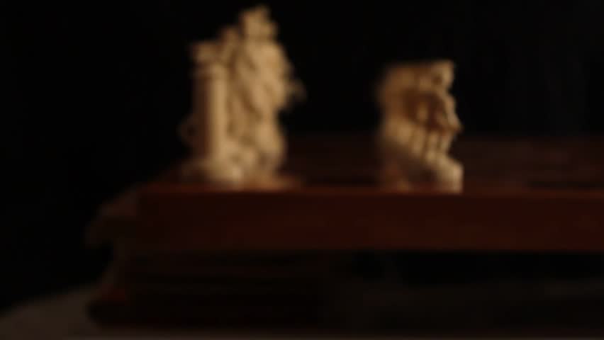 Macro shot of Greek mythology-themed chess pieces. A hand moves the Queen, setting the stage for strategic gameplay. Dramatic lighting enhances the carved detail.