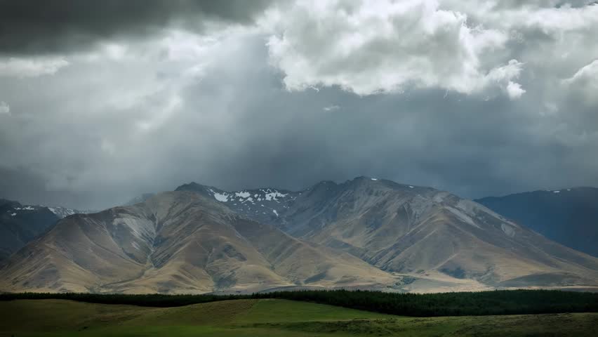 Expansive view of rugged mountains under a turbulent sky with visible rain streaks and dramatic cloud formations