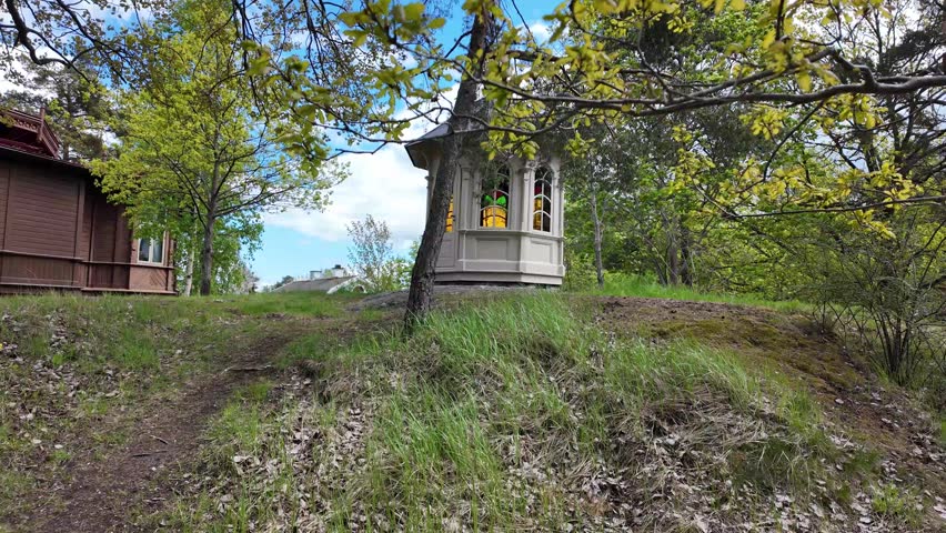 Historic wooden buildings in a green park setting with tree branches moving in the wind. Peaceful Scandinavian heritage scene with traditional architecture and nature.
