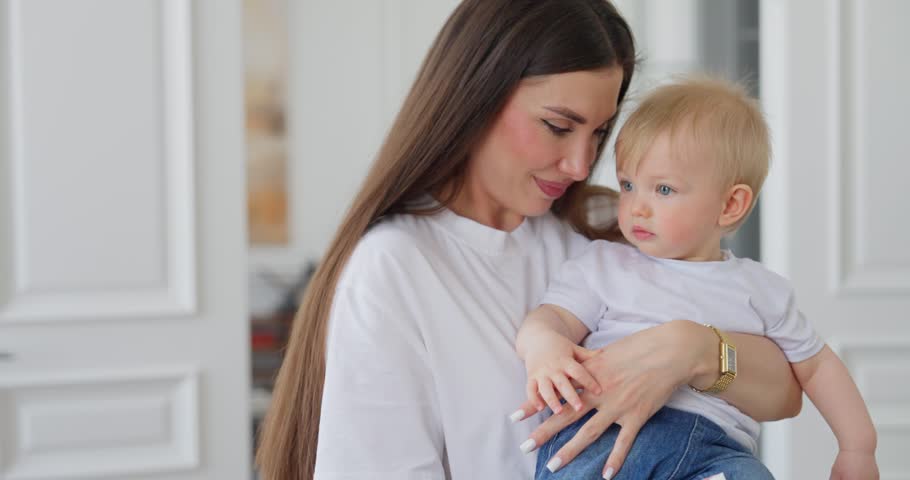 Tender portrait of a young mother gently holding her baby in a bright modern home, sharing a calm affectionate family moment in soft natural light