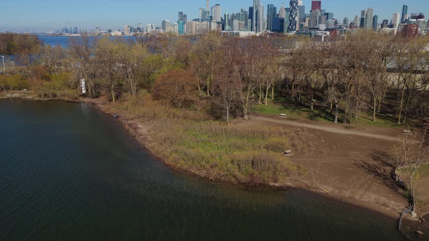 Scenic Toronto skyline showcasing downtown buildings and iconic CN Tower from Toronto Islands park with tranquil Lake Ontario waterfront and clear blue sky during springtime