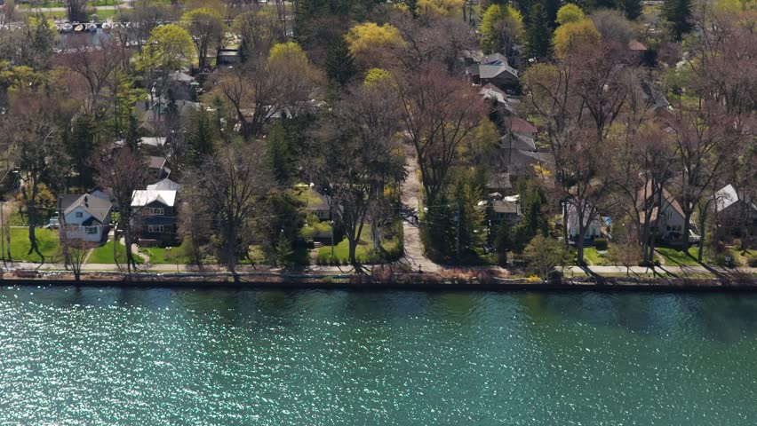 Scenic aerial traveling revealing Toronto Islands neighborhood with homes, cottages, vacation rentals surrounded by trees and green spaces along the waterfront