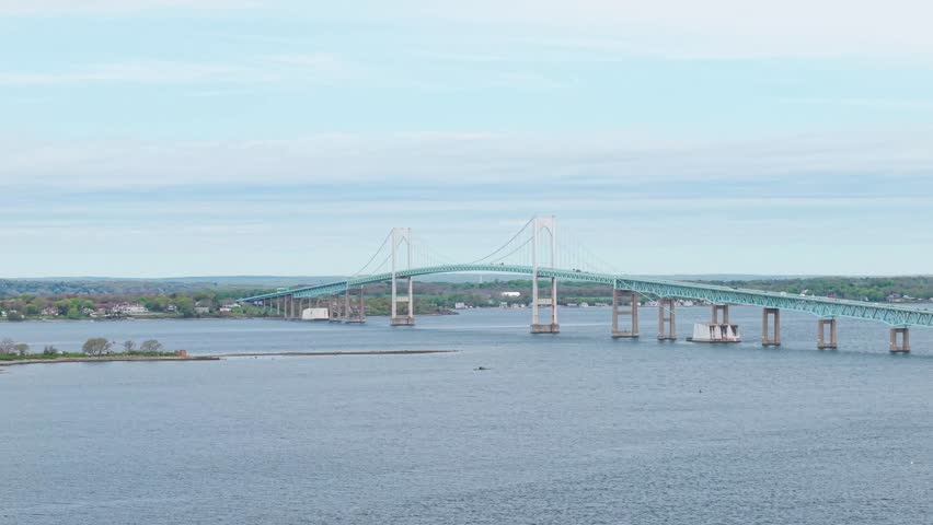 Claiborne Pell Newport Bridge wide aerial view, a distant scenic drone tracking shot showcasing the massive green suspension bridge spanning across the open waters of Narragansett Bay in Rhode Island.