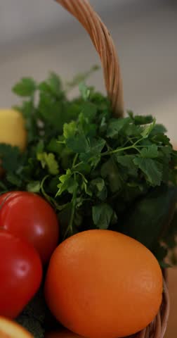 Fresh vegetables and fruits in wicker basket on table indoors, closeup. Camera moving