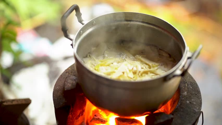 Outdoor cooking pot on wood fire with boiling soup and flame, rustic kitchen stove meal with ginger steam, traditional countryside food close up
