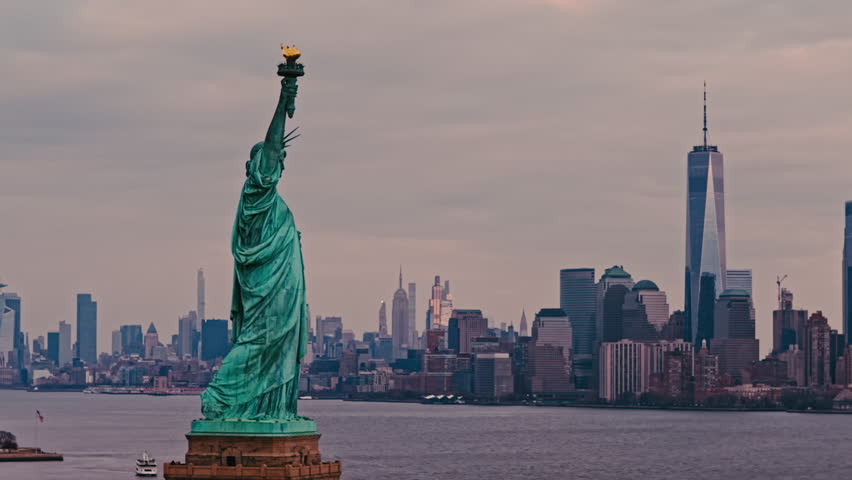 Aerial cityscape with Liberty statue and Manhattan skyline. Drone shot of Liberty statue and NYC skyline. Aerial perspective of Liberty statue over New York City.