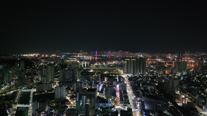 Aerial view over the illuminated Busan cityscape and harbor, night in South Korea
