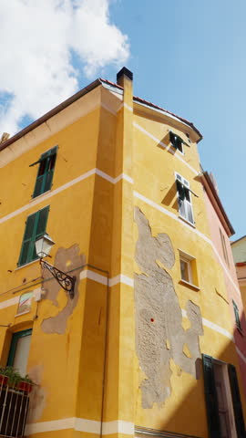 Upward pan of rustic yellow building with weathered walls under sunny blue sky