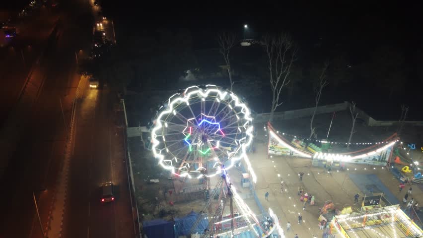 Illuminated ferris wheel glows brightly at night in a fairground as people walk around the attraction during this festive event.