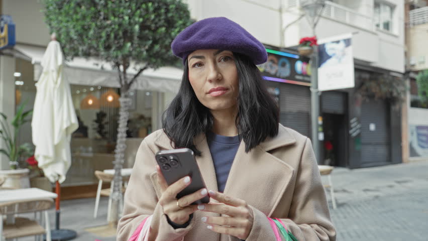 Young woman holding shopping bags and checking smartphone while touching temple on a street; concern consumer stress.