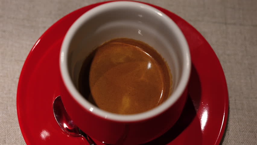 Fresh espresso coffee served in a red ceramic cup with crema on top in a cafe setting