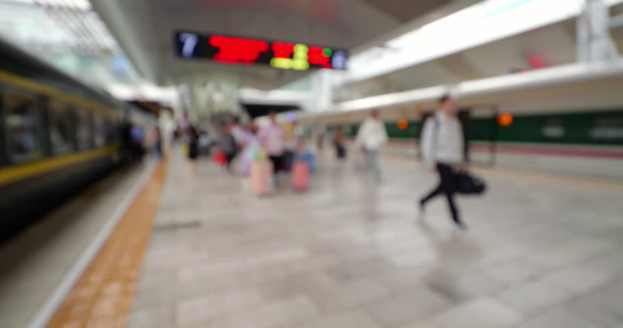 Blurred view of diverse flow of passengers carrying luggage walking along a busy platform at Kunming railway station between a classic green locomotive and a modern bullet train, wide-angle shot, defocused to ensure safe commercial usage.
